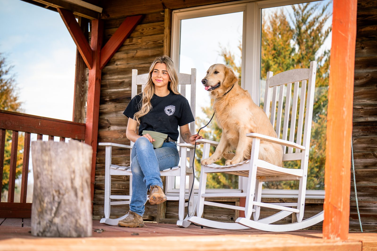 A trainer sitting on a log-cabin porch beside a golden retriever